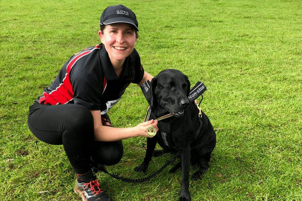Runner, Nicola, is crouched beside black Labrador, Lola, after winning their canicross race.